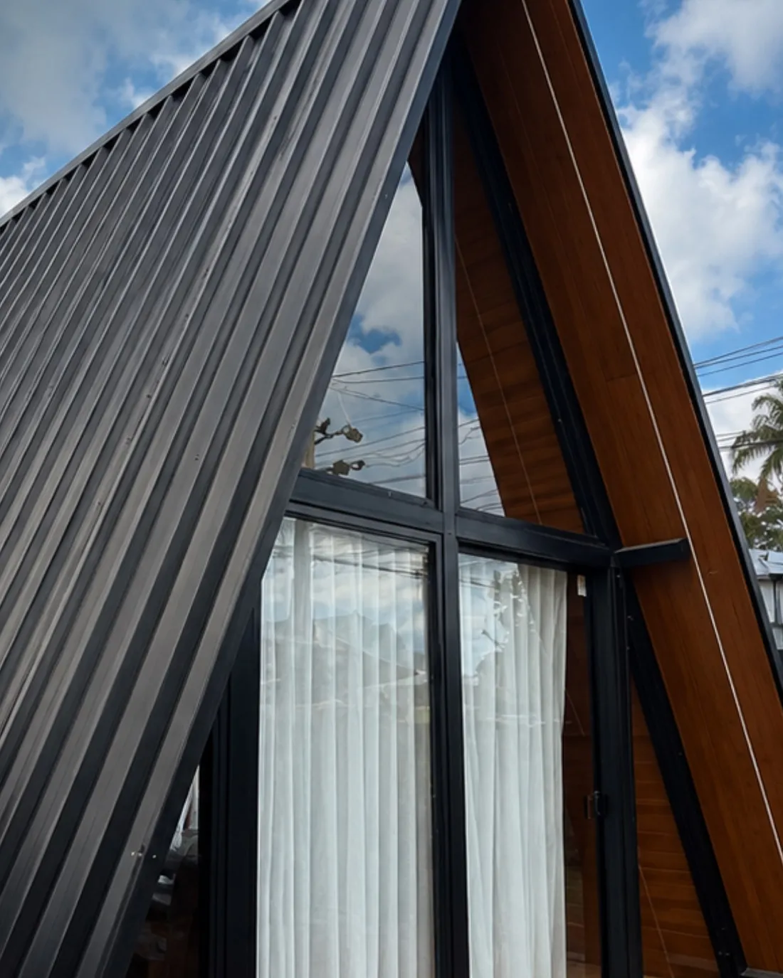 Chalé A-frame com cobertura em telha trapezoidal preta, frente envidraçada com cortina e lateral em madeira